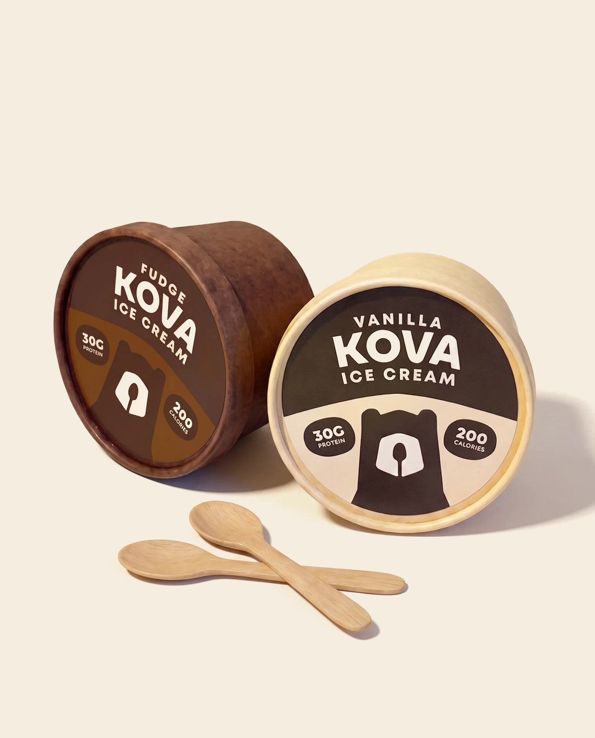 Kova Fudge and Vanilla protein ice cream cups with wooden spoons on a cream background