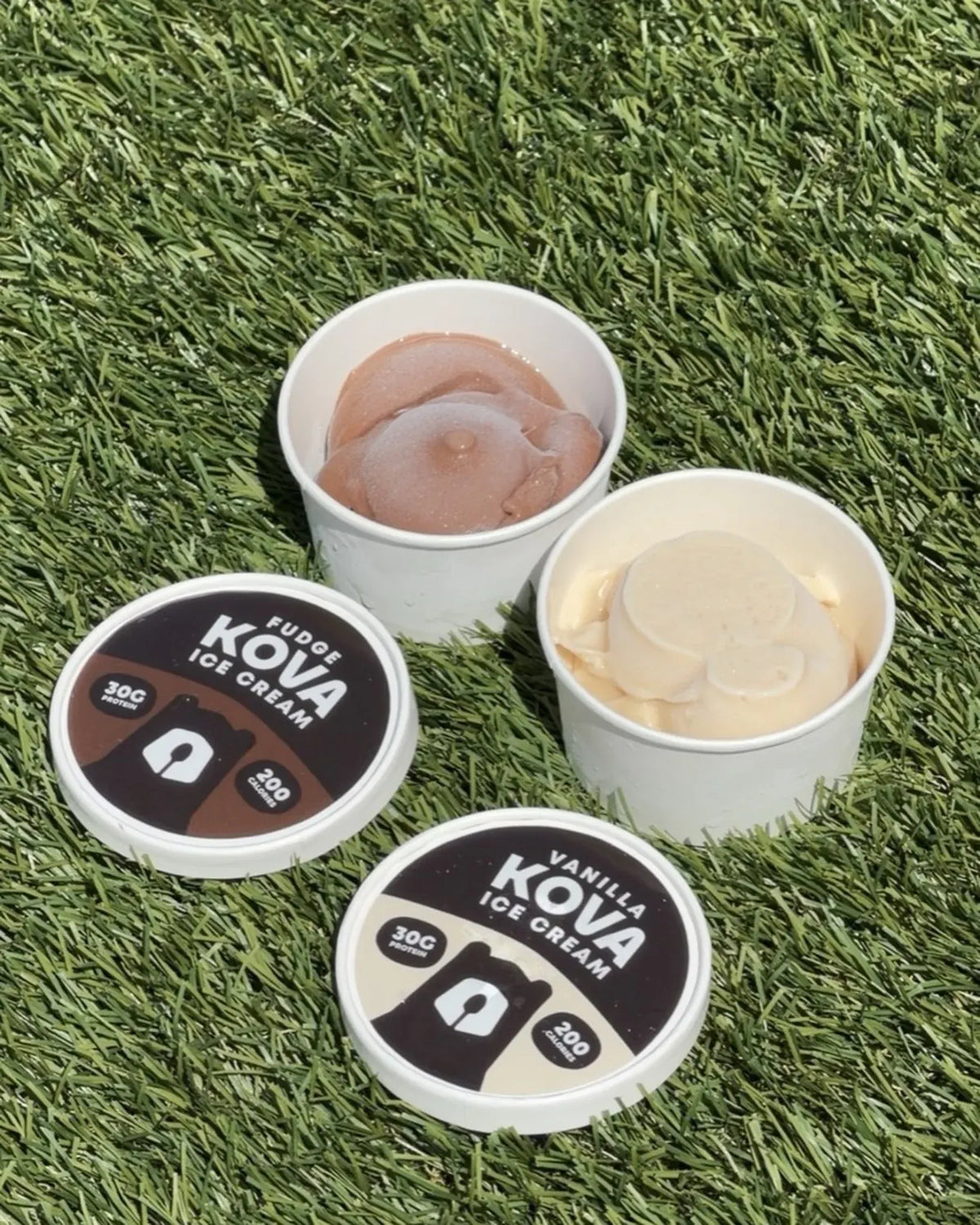 Two open cups of Kova protein ice cream, fudge and vanilla, with their lids on the turf at a Los Angeles pop-up