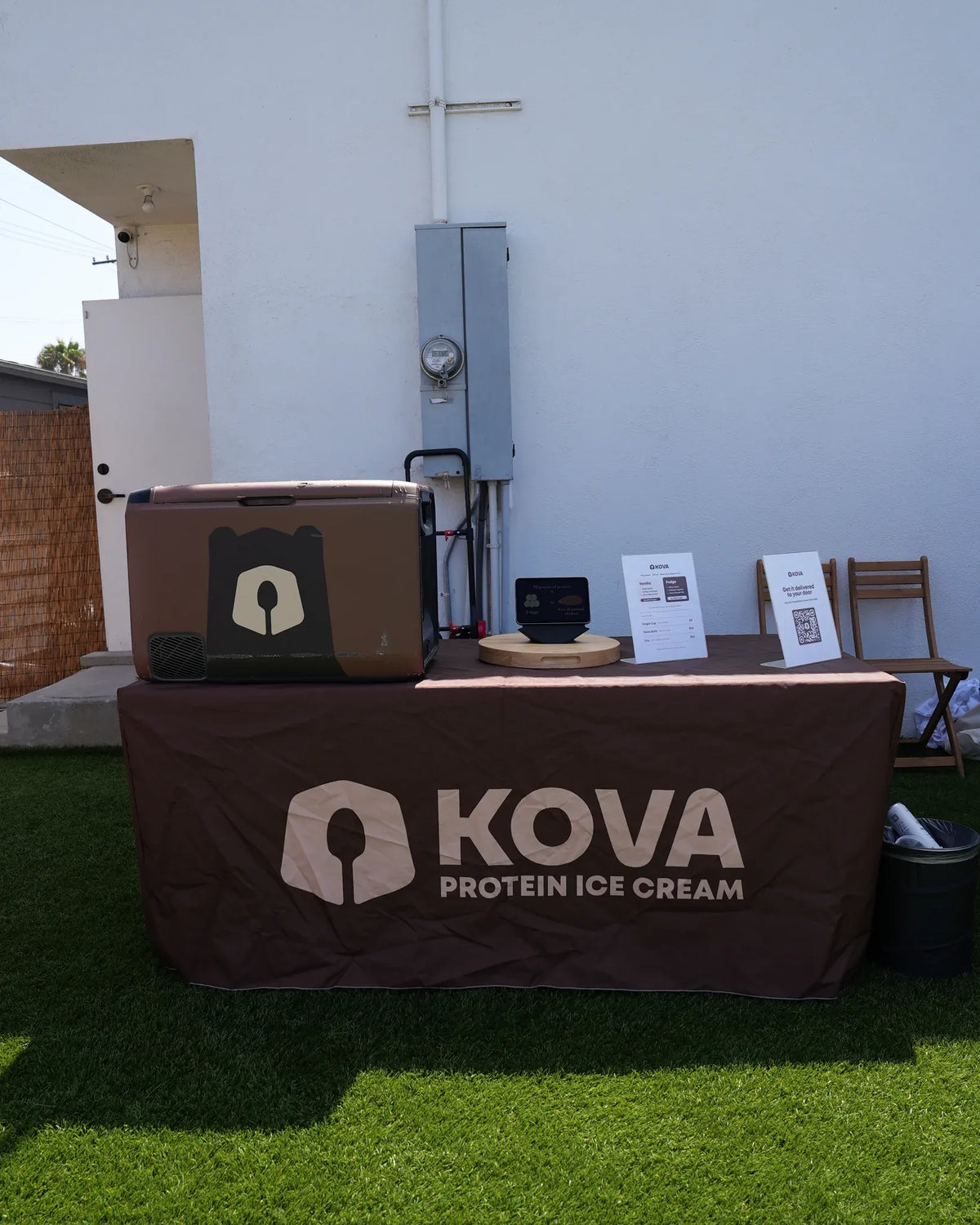 The Kova pop-up table on turf, with its branded cover, travel freezer and flavor signage, set up outside a Los Angeles studio